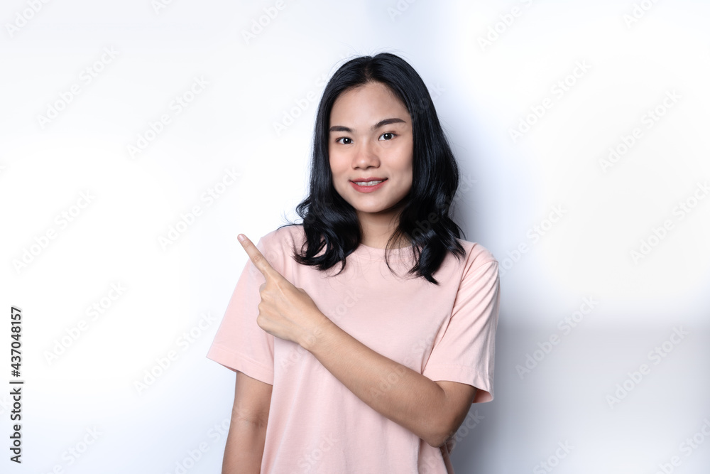 Portrait of young beautiful Asian woman pointing hand as in gesture of presenting something with open smile to camera with self-confident and friendly manner. Female rising a finger up having an idea. Portrait of young beautiful Asian woman pointing hand as in gesture of presenting something with open smile to camera with self-confident and friendly manner. Female rising a finger up having an idea.
