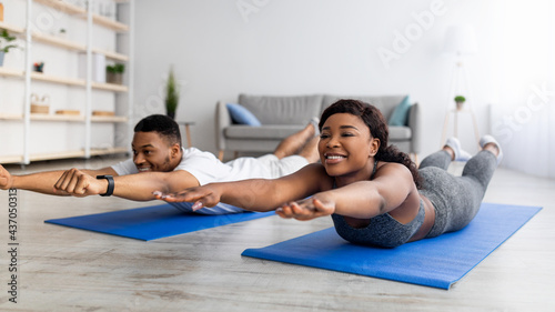 Home trainings during covid lockdown. Strong black couple exercising on sports mats, doing yoga or pilates indoors