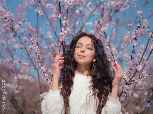 A beautiful young woman near a blooming spring pink tree