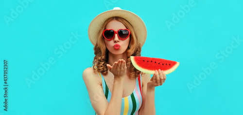 Summer portrait of young woman blowing her lips with red lipstick sending a kiss with slice of watermelon on blue background