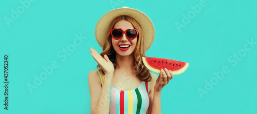 Summer portrait of happy smiling young woman with slice of watermelon wearing a hat on blue background