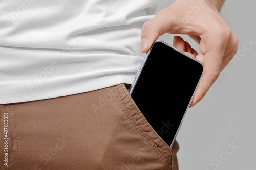 Close up of male hand taking out big mobile phone with empty black screen from front pocket of brown pants on grey background. photo