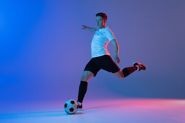 Young Caucasian man, male soccer football player training isolated on gradient blue pink background in neon light