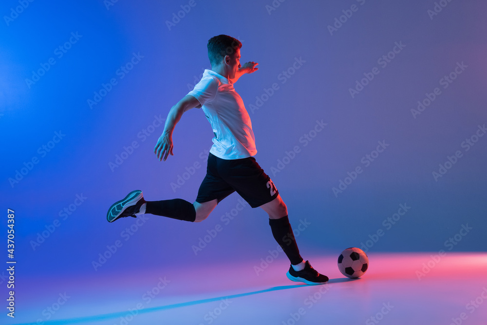 One male soccer football player in action and motion isolated on gradient blue pink background in neon light