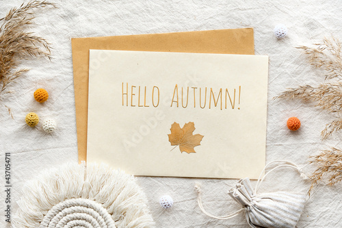 Text Hello Autumn on white card with envelope. Off white textile flat lay with macrame and dry reeds, pampas grass. Franrance bag with Autumn aroma. Simple minimal flat lay with natural light.