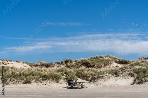 Fototapeta Naklejka Na Ścianę i Meble -  two bicycles parked in front of a large sand dune covered in grasses and reeds under a blue sky