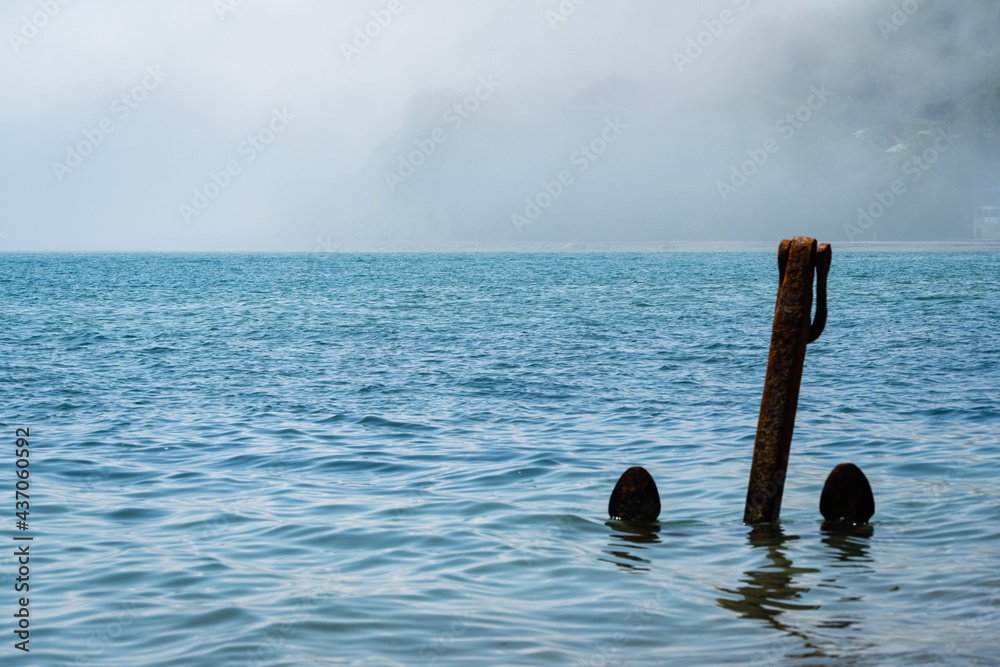 Large anchor stands upright in shallow water near shore. Beach in Arkhipo-Osipovka. Close-up. Anchor is rusty. Cloud descended over sea water. Sea water of emerald color. Black Sea coast of Caucasus. Large anchor stands upright in shallow water near shore. Beach in Arkhipo-Osipovka. Close-up. Anchor is rusty. Cloud descended over sea water. Sea water of emerald color. Black Sea coast of Caucasus.