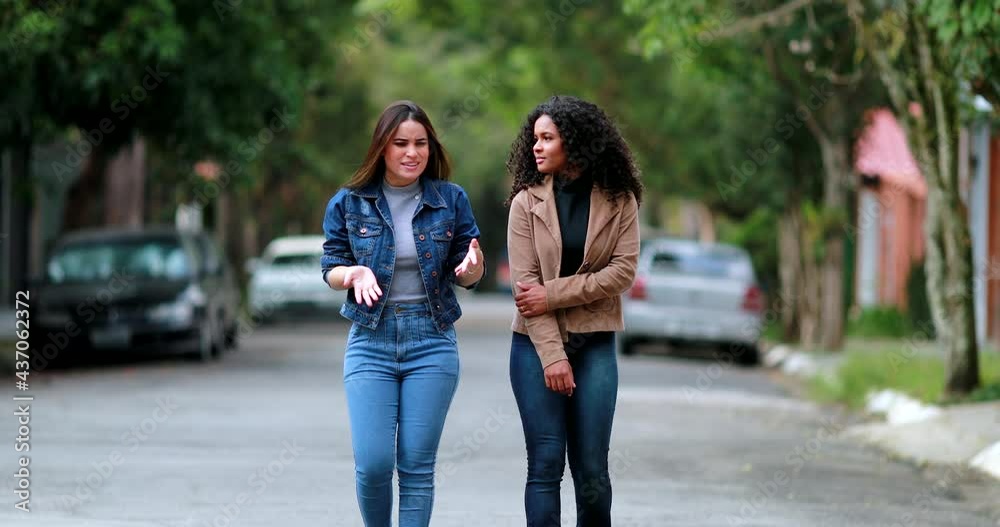 Two women walking together in conversation. Diverse girlfriends speaking in street walk