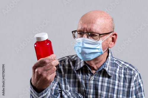 Old bald man with glasses and medical mask with red jar of pills in his hand. Copy space.
