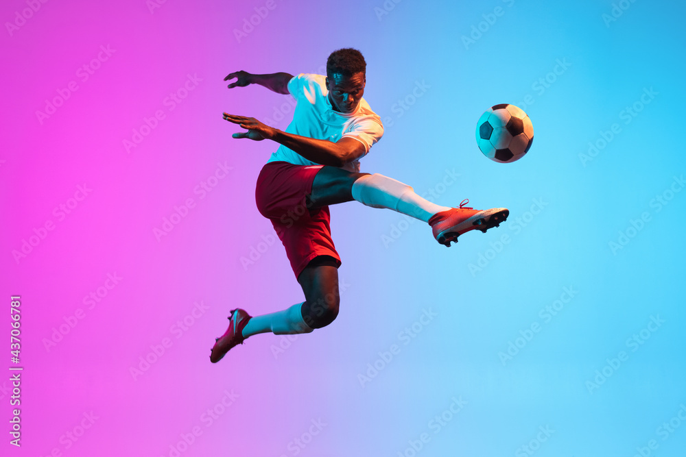 Naklejka One African man, professional soccer football player training isolated on gradient blue pink background in neon light.