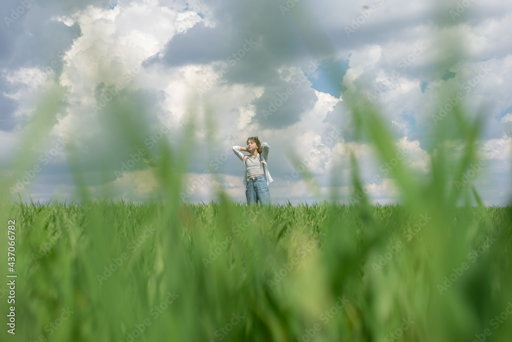 Obraz premium teenage girl in green grass, in the field, against the backdrop of a cloudy sky