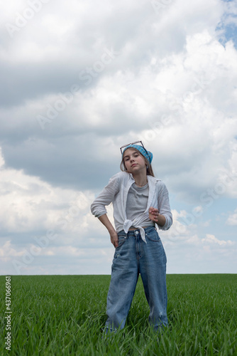 portrait of a little teenage girl in a field of green grass, against the backdrop of a cloudy sky