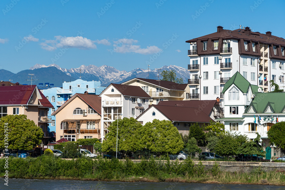 Residential buildings in federal territory of Sirius against backdrop of snow-capped peaks. Caucasus mountains. Imeretinskaya lowland. In foreground is Mzymta.Adler. Sochi, Russia - May 18, 2021 Residential buildings in federal territory of Sirius against backdrop of snow-capped peaks. Caucasus mountains. Imeretinskaya lowland. In foreground is Mzymta.Adler. Sochi, Russia - May 18, 2021