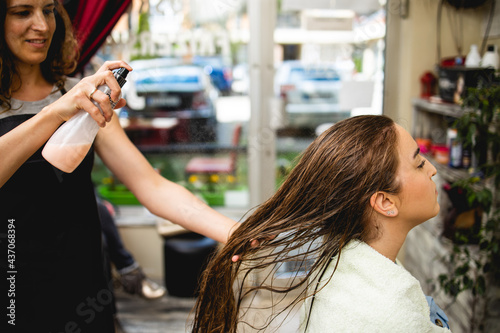 Hairdresser drying hair of a beautiful young adult woman in hair salon.