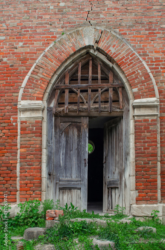 Entrance to the old abandoned church of red brick, broken doors © romankrykh