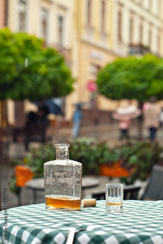 Bottle of alcohol near a glass on an empty table. The concept of alcoholism  loneliness and depression. Old vintage bottle on a checkered tablecloth. Blurred city street on background.