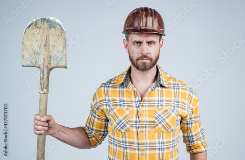 man laborer in construction safety helmet and checkered shirt on building site with shovel, industry