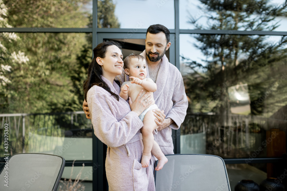 Portrait of a young family with a one year baby boy resting at Spa resort, hug together near the sauna outdoors. Parents with a newborn son on vacation