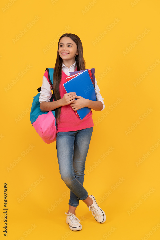 happy teen school girl with backpack and copybook on yellow background, knowledge