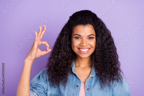 Photo of cute adorable dark skin woman dressed jeans shirt smiling showing okey sign isolated violet color background