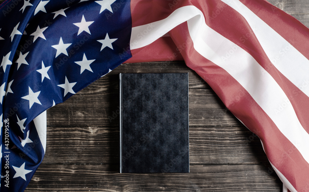 Obraz premium United States of America flag. Black book on a wooden background. Constitution. Guarantee of democracy.