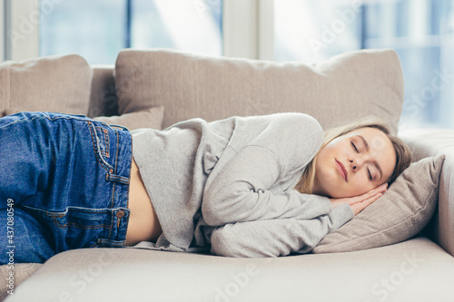 Young woman sleep resting at home on couch after a hard day's work. Relax calm and rest. On a soft cozy comfortable sofa. Comfort safety. Female with closed eyes feels comfortable and safe in warmth 