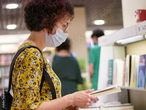 A woman looking at books in a bookstore wears a face mask