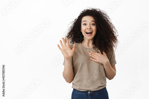Hello its me. Happy young woman raising hand and name herself, holding palm on heart, introduce her to you, standing friendly and joyful against white background