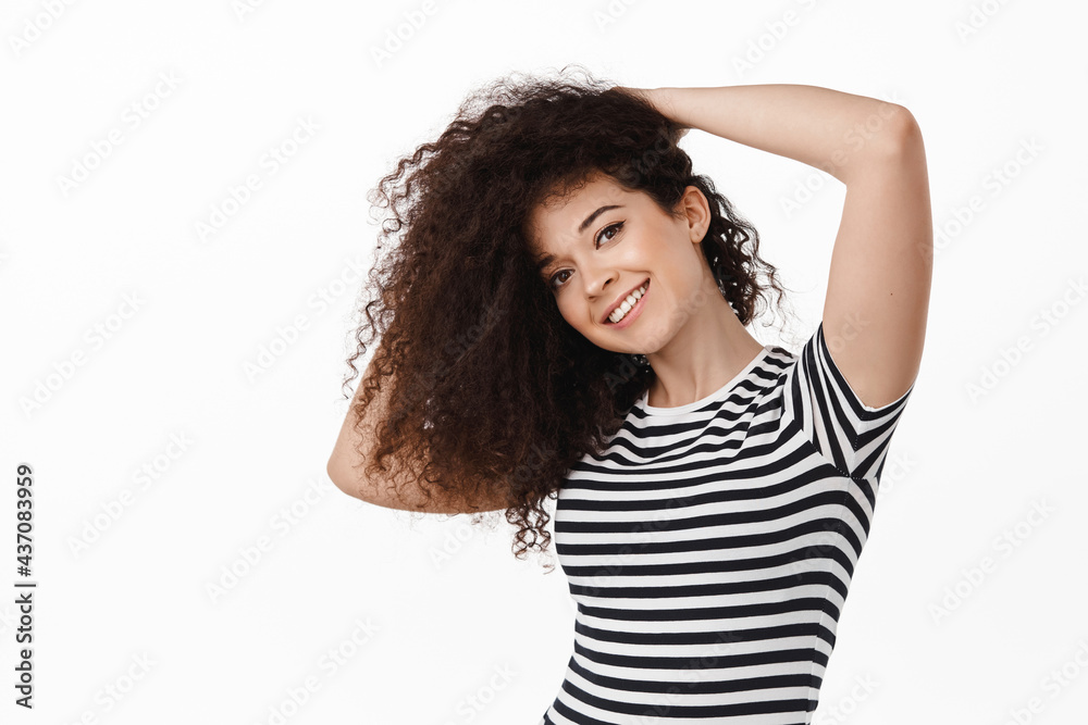 Beauty. Young attractive brunette woman with curly long healthy hair, whip hairstyle and smiling, taking care of haircut, standing against white background Beauty. Young attractive brunette woman with curly long healthy hair, whip hairstyle and smiling, taking care of haircut, standing against white background