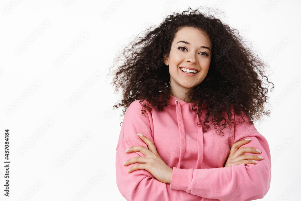 Close up portrait of confident brunette woman in casual hoodie, cross arms on chest, smiling and looking happy, standing against white background Close up portrait of confident brunette woman in casual hoodie, cross arms on chest, smiling and looking happy, standing against white background