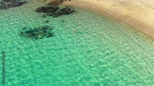 Aerial shot of young woman bathing alone in transparent turquoise water at beautiful Tuerredda beach in South Sardinia, Italy on sunny day photo