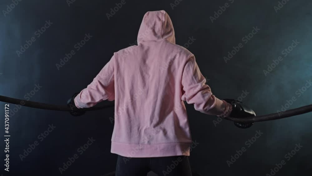 A fighter girl in a pink hoodie is warming up by holding on to the ropes A fighter girl in a pink hoodie is warming up by holding on to the ropes