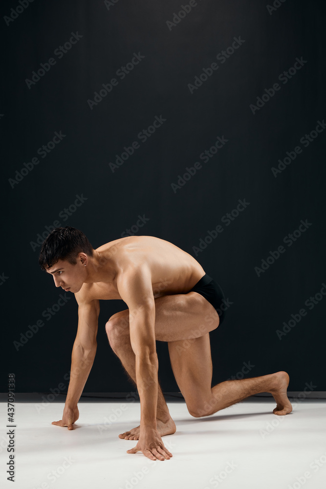 bodybuilder in black shorts stands on his knee against a dark background bodybuilder in black shorts stands on his knee against a dark background