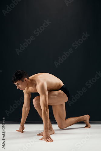 bodybuilder in black shorts stands on his knee against a dark background