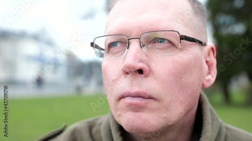 Mature man in glasses looking at street city life with anxiety and closing his eye to become relaxed and calm down. Closeup portrait outdoors. photo