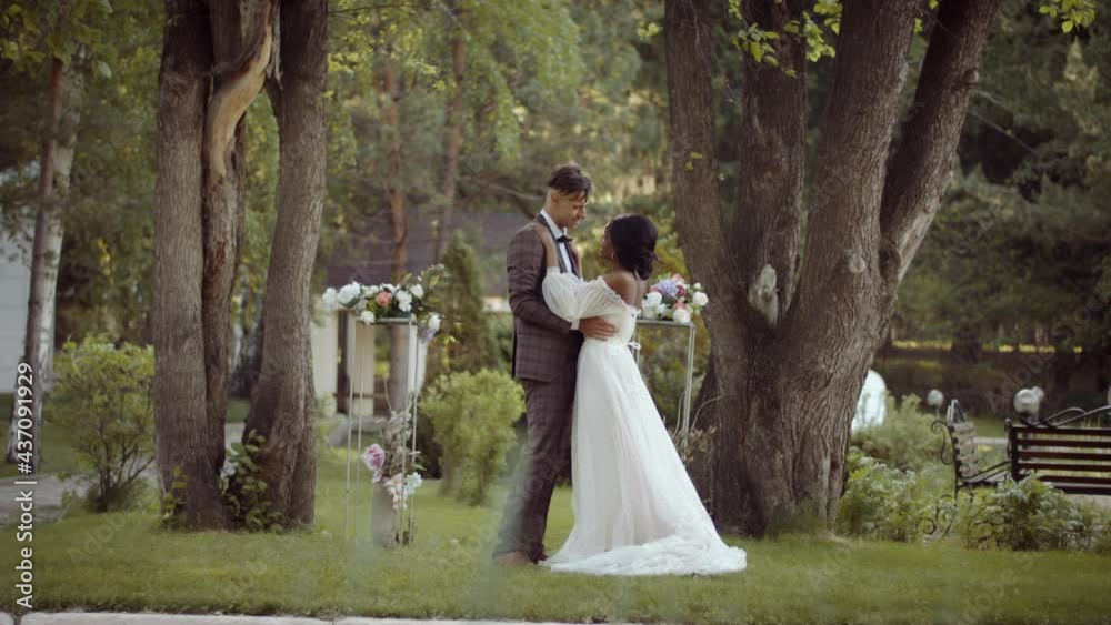Wedding of a multi ethnic couple. The bride and groom dance a slow dance after the wedding ceremony in a summer park on the grass Wedding of a multi ethnic couple. The bride and groom dance a slow dance after the wedding ceremony in a summer park on the grass