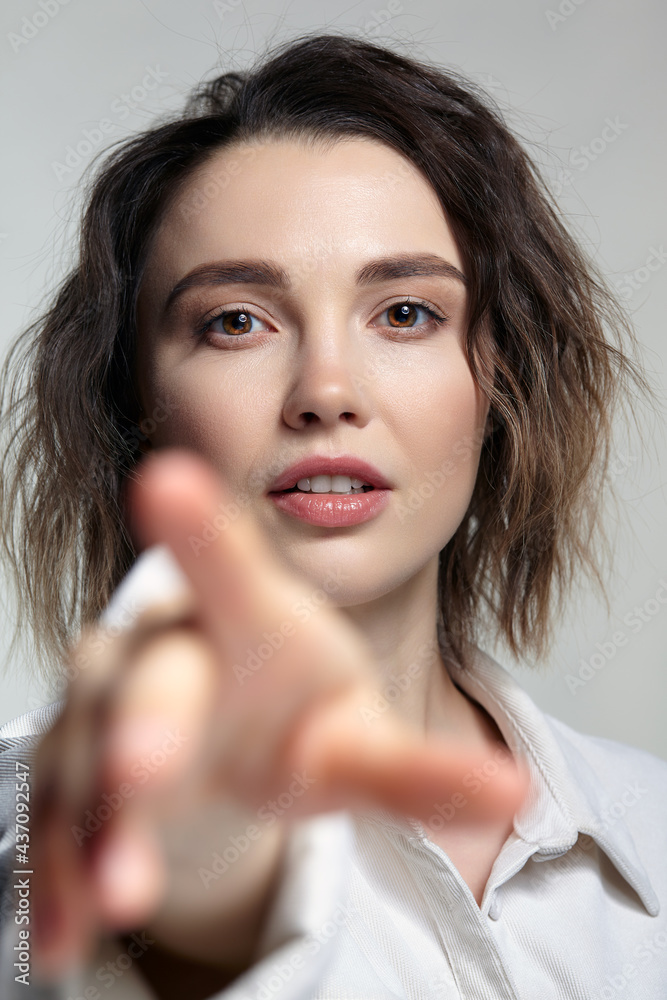 Portrait of young woman with hand stretched forward. Female posing in milky white corduroy shirt. Portrait of young woman with hand stretched forward. Female posing in milky white corduroy shirt.