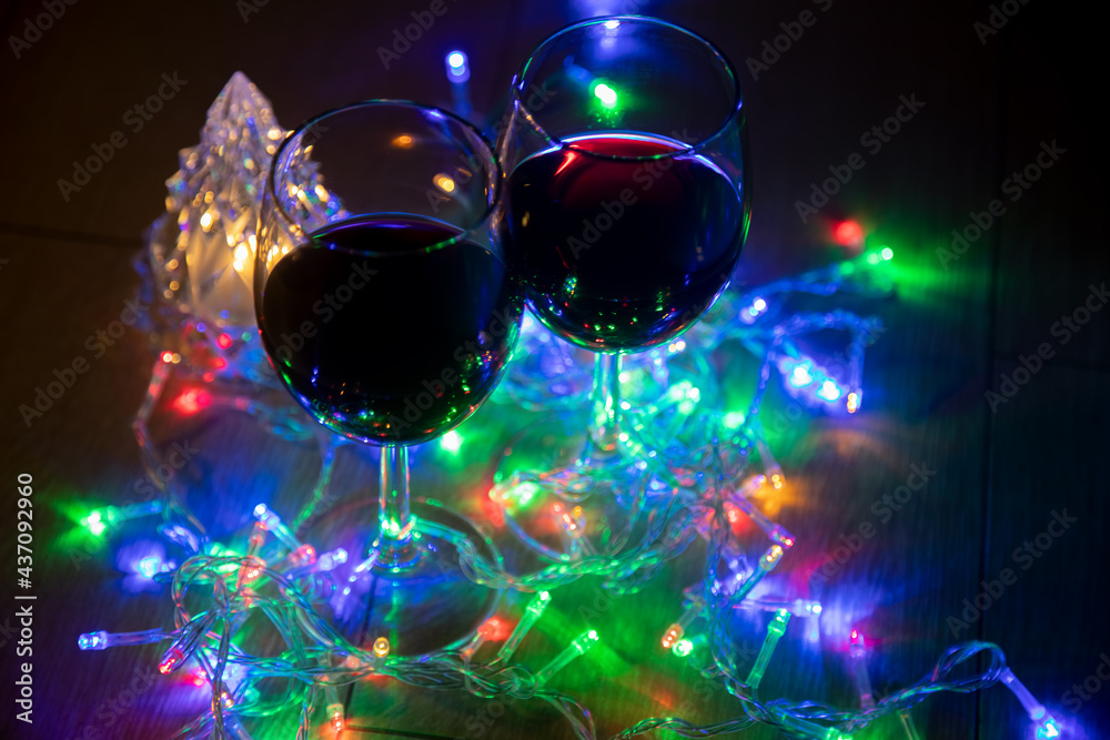 two glasses on the background of a shining Christmas tree and a multi-colored garland on a dark night background. New Year celebration. two glasses on the background of a shining Christmas tree and a multi-colored garland on a dark night background. New Year celebration.