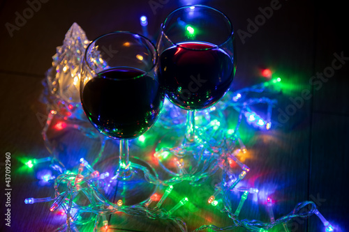 two glasses on the background of a shining Christmas tree and a multi-colored garland on a dark night background. New Year celebration.