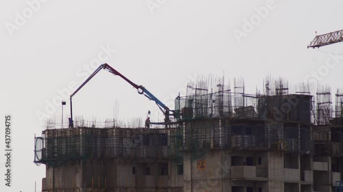 construction site on the rooftop of a tower skyscraper with rebar bars stiking out and construction crane and concrete pouring machine with workers moving around in Gurgaon, Delhi, India photo