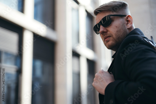 Handsome male tourist in a coat and with a backpack in sunglasses looks to the side and walks around the city