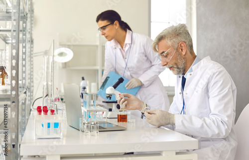 Medical scientists working in science laboratory and analyzing samples using modern lab equipment. Serious mature man doing advanced research in field of chemistry, medicine, biology or pharmaceutics