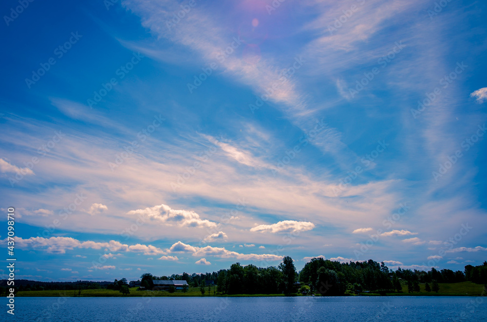 Landscape of a lake with blue sky, pink and white clouds and woodland in the background Landscape of a lake with blue sky, pink and white clouds and woodland in the background