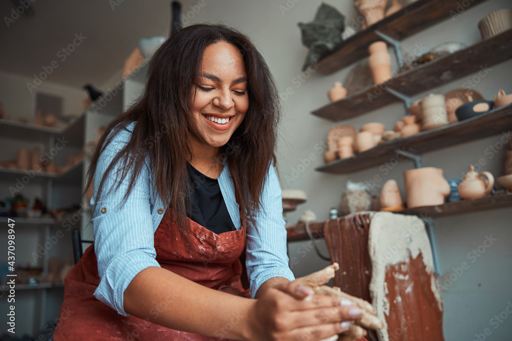 Cheerful woman ceramist making pottery in workshop