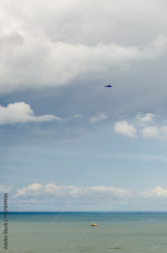 A police helicopter in the sky, hovering above a small boat on the sea below A police helicopter in the sky, hovering above a small boat on the sea below