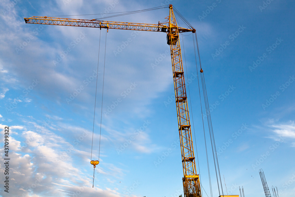 Tower crane of yellow color at a construction site against the background of the sky, bottom view. Tower crane of yellow color at a construction site against the background of the sky, bottom view.