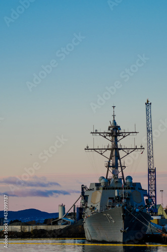 An American military ship docked in a foreign harbor with sunset light in the background and industrial buildings © Gunnar Sommerfeldt
