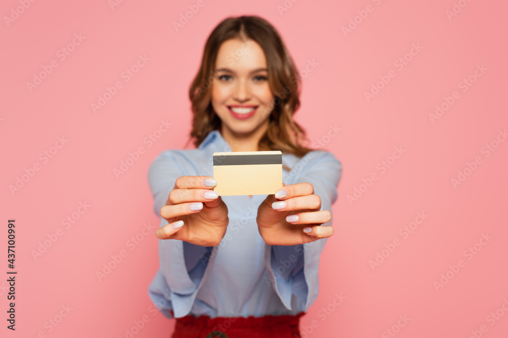 Credit card in hands of smiling woman on blurred background isolated on pink Credit card in hands of smiling woman on blurred background isolated on pink