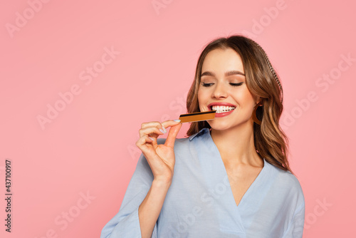 Pretty woman biting credit card isolated on pink