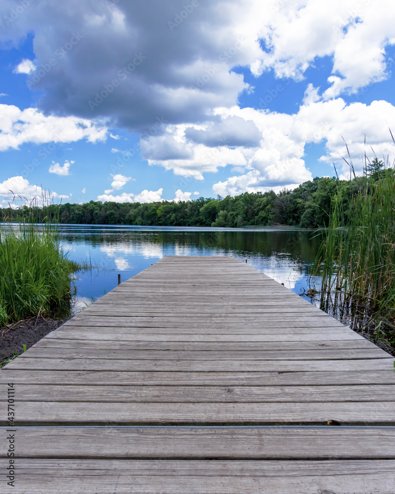 Looking down the boat pier on Upper Genesee Lake in Waukesha County, Wisconsin. Lazy cumulus clouds are reflected in the calm lake waters. Looking down the boat pier on Upper Genesee Lake in Waukesha County, Wisconsin. Lazy cumulus clouds are reflected in the calm lake waters.